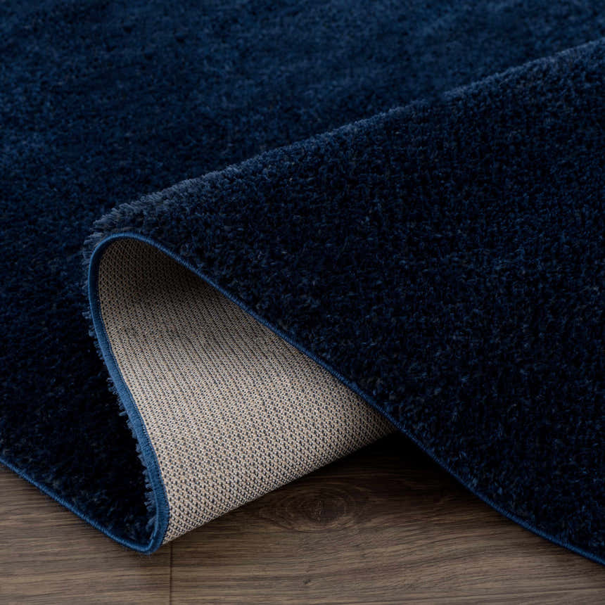 Close-up of the plush, dark blue Navero rug showing its texture and backing on a wood floor. Fold