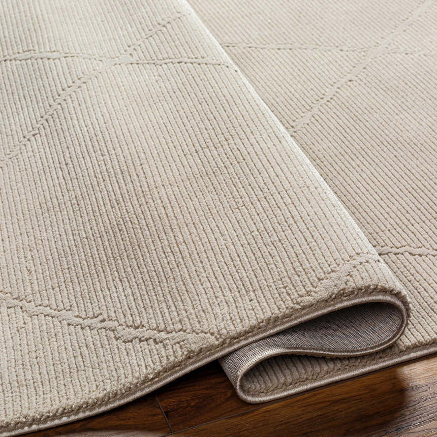 Close up of the Aldis Tan Plush Textured Washable Rug showing its plush pile, geometric design, and bound edge. Fold