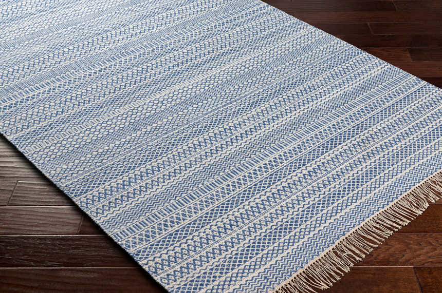 Close-up of the Sanc Blue/Cream Flatweave Wool Rug showing its geometric pattern and fringe on dark wood flooring. Corner