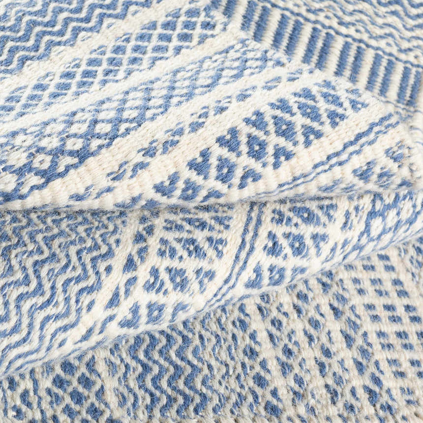 Close-up of the Sanc Blue/Cream rug showing the flatweave texture and geometric pattern in blue and cream wool. Fold