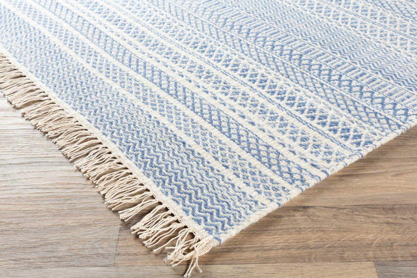 Close-up of the Sanc Blue/Cream rug showing its flatweave texture, geometric pattern, and fringe detail on a wood floor. Front