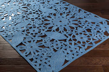 Close-up of the blue Sauquoit Area Rug showing its hand woven floral and leaf pattern on a dark wood floor. Corner