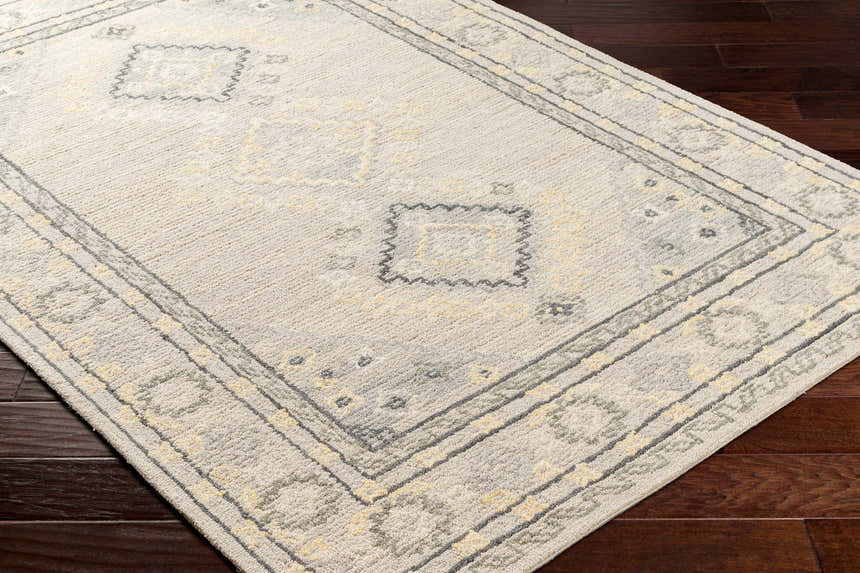 Close-up of the hand-tufted Alena Gray Wool Blend Area Rug featuring a traditional gray and yellow geometric pattern. Corner