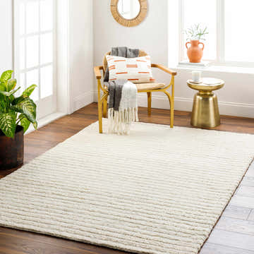 Bright room scene with a textured off-white Debra Area Rug, wood floors, gold side table, and a woven chair. Roomscene-Rectangle