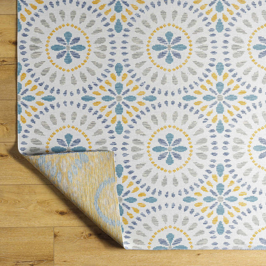 Close-up of the Karin Area Rug. Light gray rug with a floral pattern in blue, gray, and yellow on a wood floor. Fold