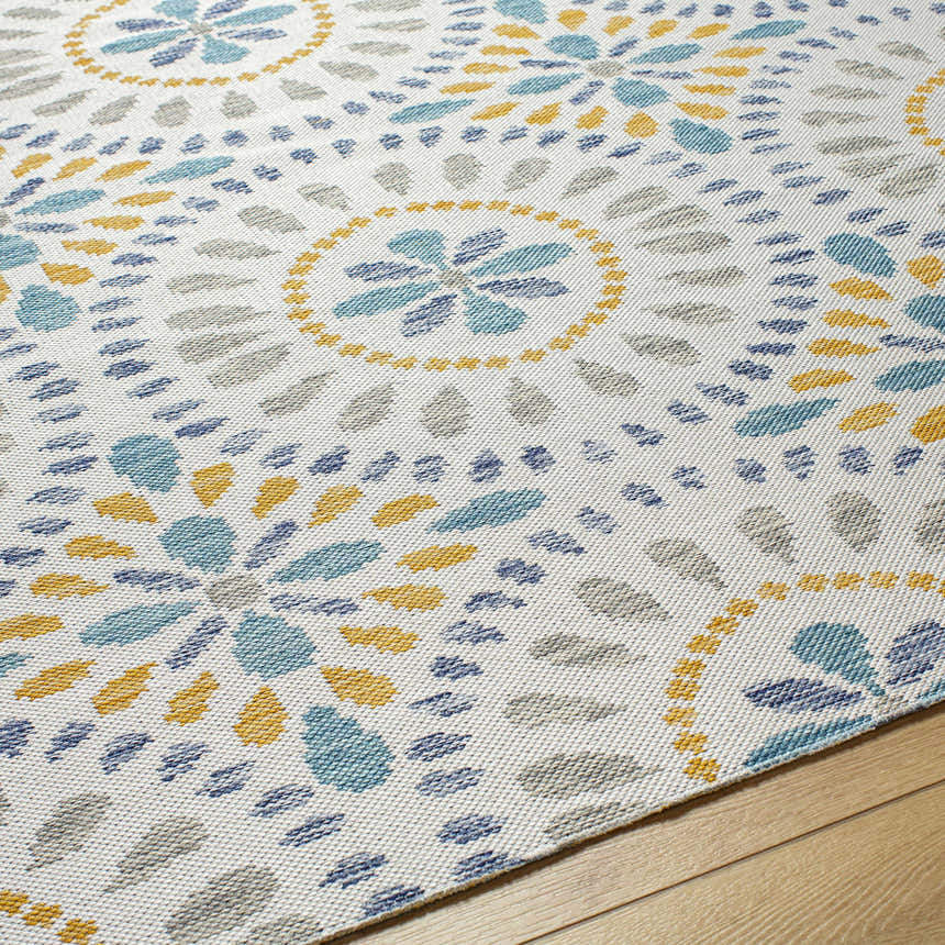 Close-up of the Karin Area Rug. Light gray rug with coastal-style floral pattern in blue, gray, and yellow. Machine woven texture. Texture