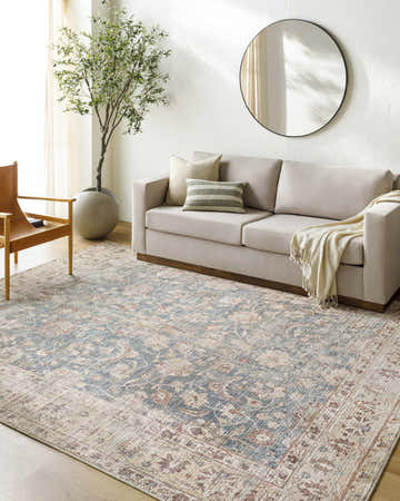 Living room scene with a Marlene Damask Beige & Navy Area Rug, beige sofa, leather chair, and potted tree. Roomscene-Rectangle
