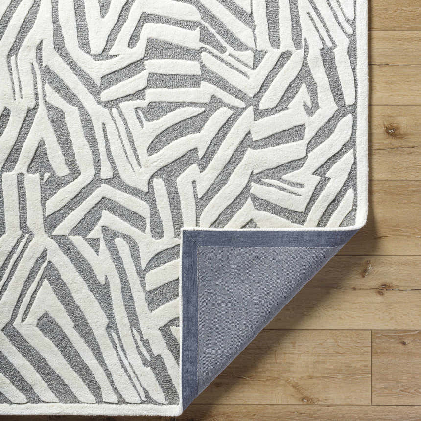 Close-up of the Avian Gray Wool Area Rug showing its cream abstract pattern and gray wool texture on a wood floor. Fold