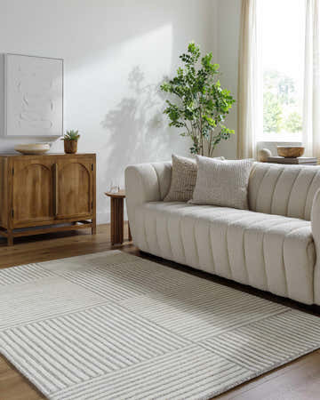 Living room scene with a cream sofa and a Coyne Cream Area Rug featuring a geometric line pattern. Roomscene-Rectangle