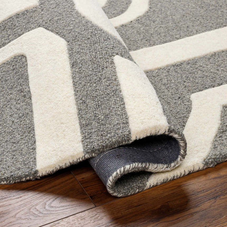Close-up of the hand-tufted Daryl Area Rug. Gray wool rug with a bold, off-white geometric pattern. Contemporary style. Fold