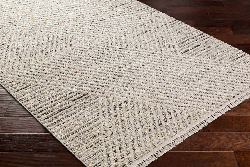 Close-up of Brita Area Rug in bone and cloud gray with a geometric pattern on dark brown wood floors. Corner