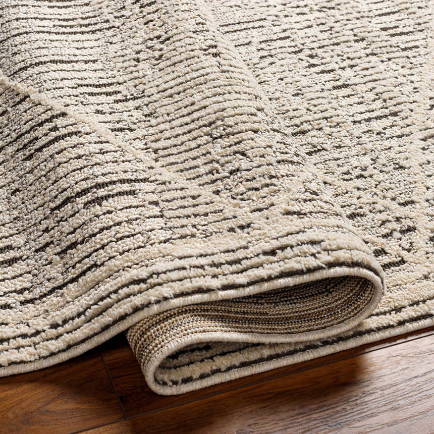 Close-up of the Luuk Area Rug showing its ivory and dark brown geometric pattern and textured, machine-woven construction. Fold