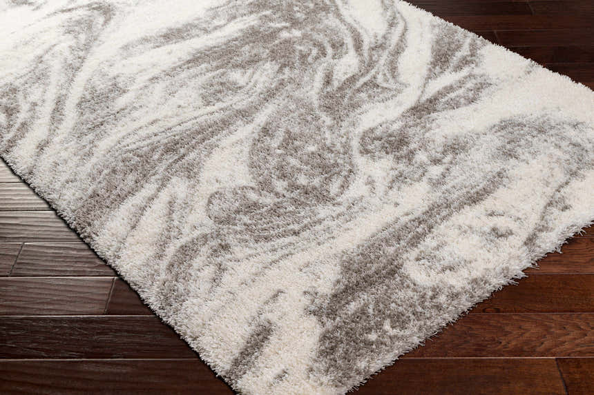 Close-up of the Delma Area Rug showing a gray and off-white swirl pattern and a soft, shag texture on dark wood flooring. Corner
