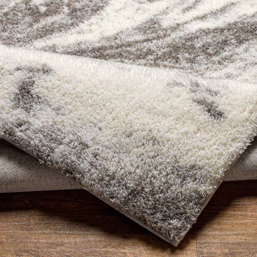 Close-up of the Delma Area Rug showing its shag texture and cloud gray, dark gray, and off-white colors. Fold