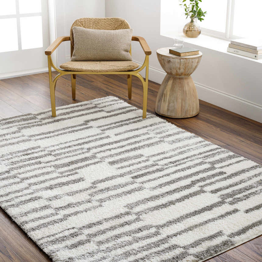Living room scene with a Kuron Area Rug, woven chair, and wood side table. The rug has a gray and off-white geometric pattern. Roomscene-Rectangle