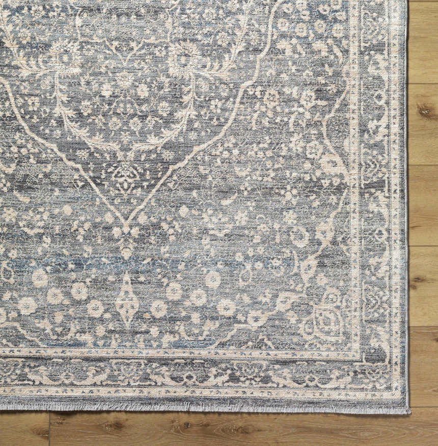 Close-up of the Anouk Area Rug. Dark gray rug with light gray traditional floral pattern on a wood floor. Corner