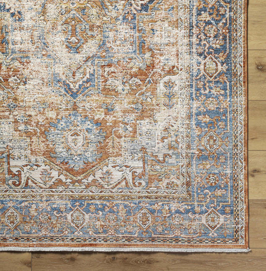 Close up of the Basim Area Rug. Traditional bone, charcoal, copper, and blue pattern on a polyester rug. Corner