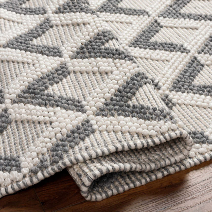 Close-up of the hand woven Maik Area Rug, showing its geometric pattern and dark gray and light gray recycled PET yarn texture. Fold