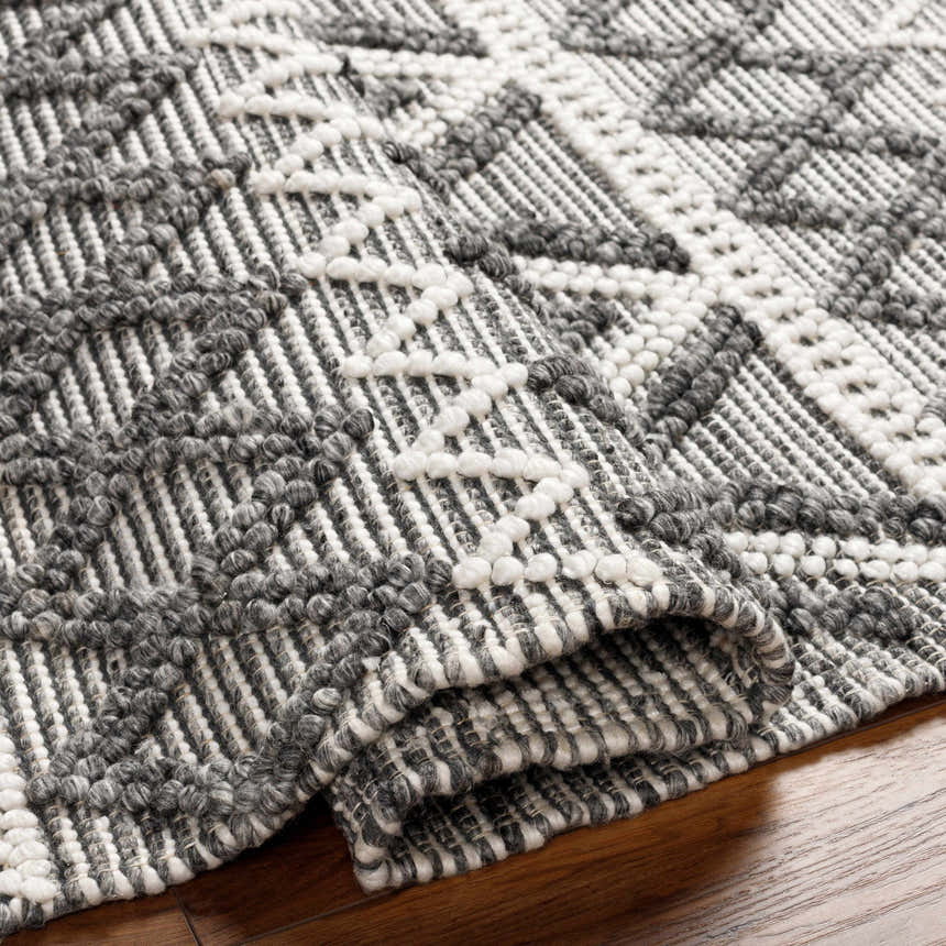 Close-up of the hand woven Yuka Area Rug. Dark gray and natural gray geometric pattern with a textured, Scandinavian style. Fold
