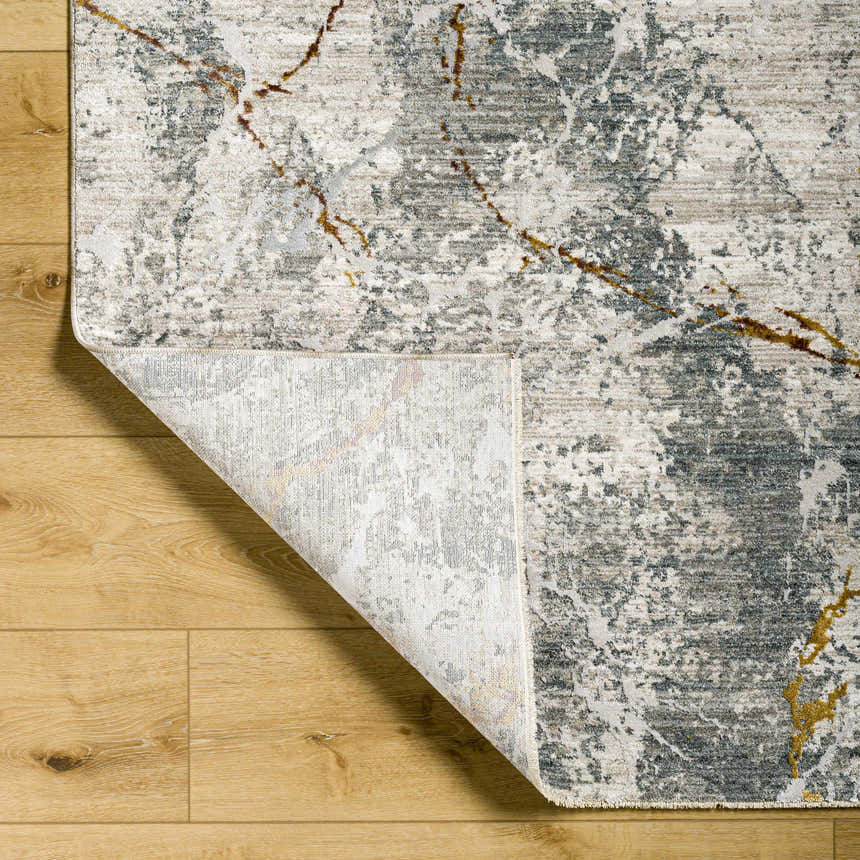 Close-up of the Asena Textured Rug. It features a contemporary gray, caramel, and brown abstract pattern on a light wood floor. Fold