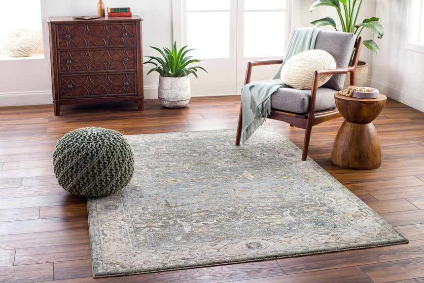 Living room scene with Aviva Teal Textured Rug, gray chair, wood accents, and a sage green pouf. Roomscene-Rectangle