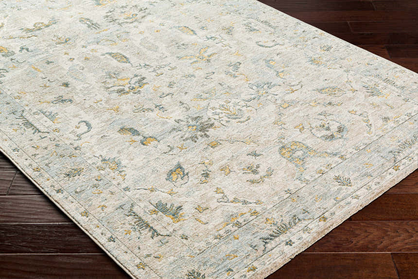 Close-up of the Emile Textured Rug with Fringes. Features a traditional floral pattern in dusty sage, light gray, and mustard tones. Corner
