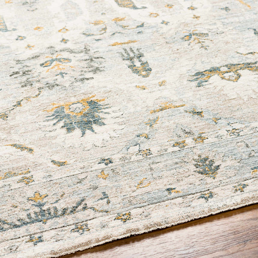 Close-up of the Emile Textured Rug with Fringes. Features dusty sage, light gray, and mustard floral patterns. Texture