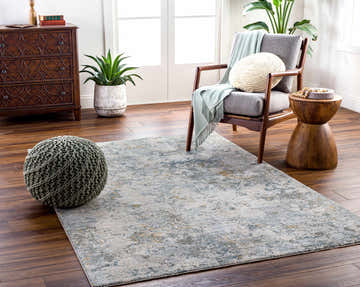 Living room scene with a Pizi Textured Rug in dusty sage, gray chair, wood accents, and green pouf. Roomscene-Rectangle