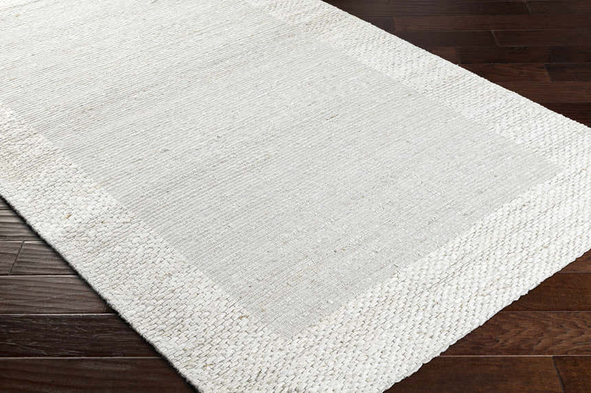 Close-up of the hand woven Jojen Off White Jute Area Rug showing the texture and design on dark wood floors. Corner
