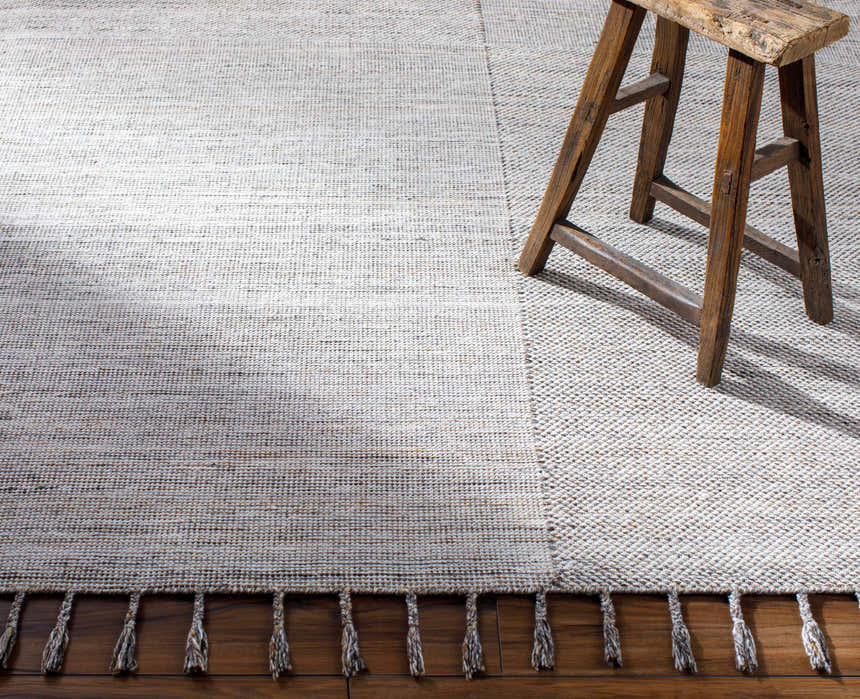 Close-up of the Anaya Beige & Teal Area Rug showing its hand-woven texture and tassel fringe detail. Rustic stool. Styleshot