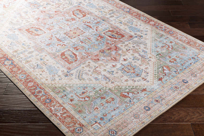Close-up of the Selbyville area rug showing its brick red, light blue, and ivory traditional pattern. Corner