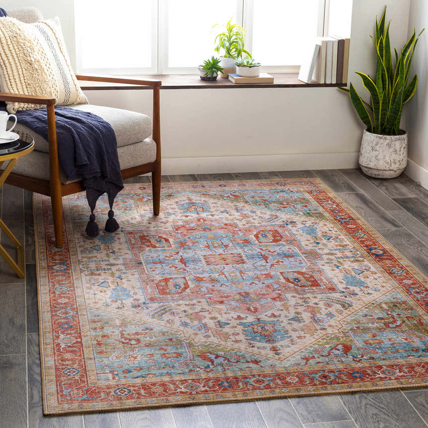 Living room scene with a Selbyville area rug in brick red, emerald, and light blue, styled with a chair and plants. Roomscene-Rectangle
