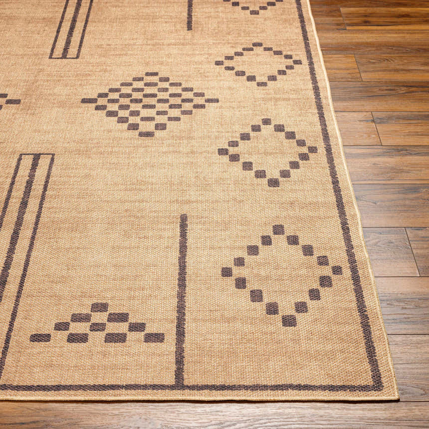 Close-up of the Fathi Washable Area Rug showing a camel color with a geometric dark brown pattern on wood flooring. Front