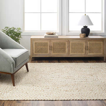 Living room scene with Elkie Cream Jute Area Rug, gray chair, wood cabinet, and natural light from windows. Roomscene-Rectangle