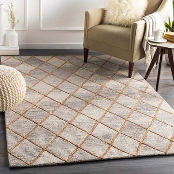 Living room scene with a beige armchair and the Sharpes Area Rug, a geometric wool rug in brown and mustard. Roomscene-Rectangle
