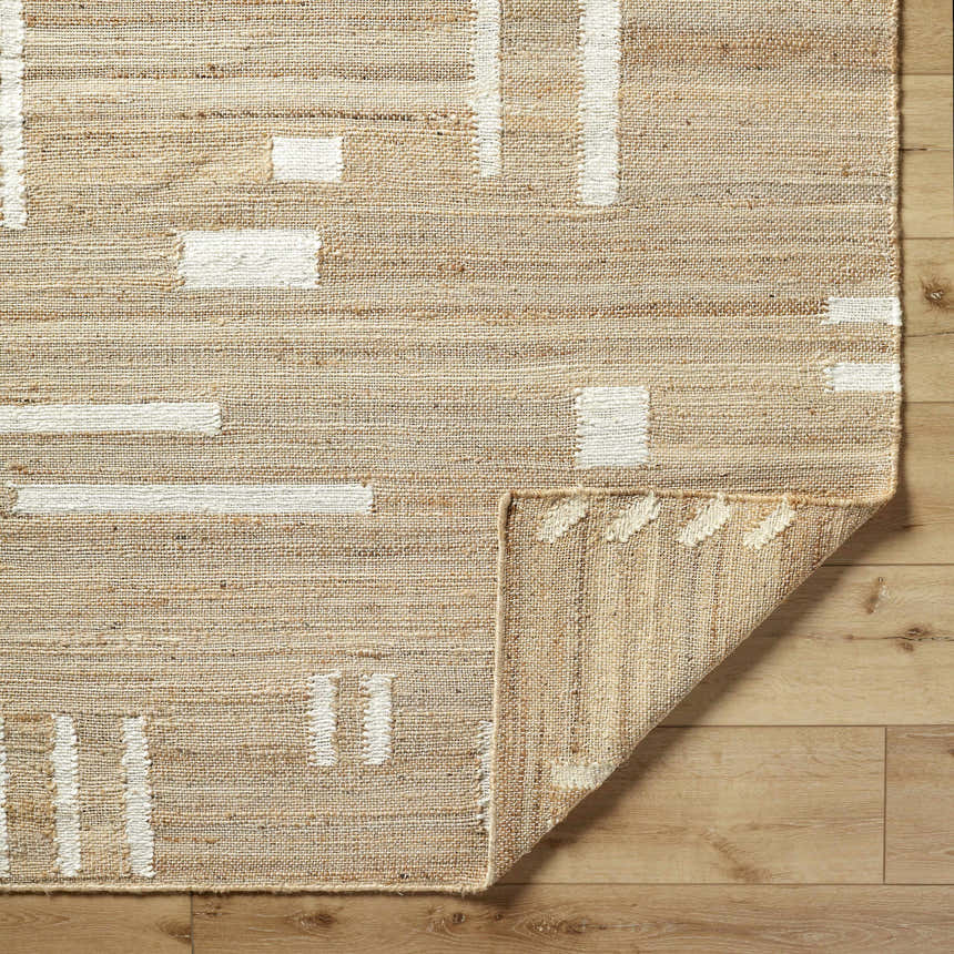 Close up of the Sasha Jute Rug showing cream geometric patterns on a tan, hand woven texture. Corner is folded to show rug backing. Fold