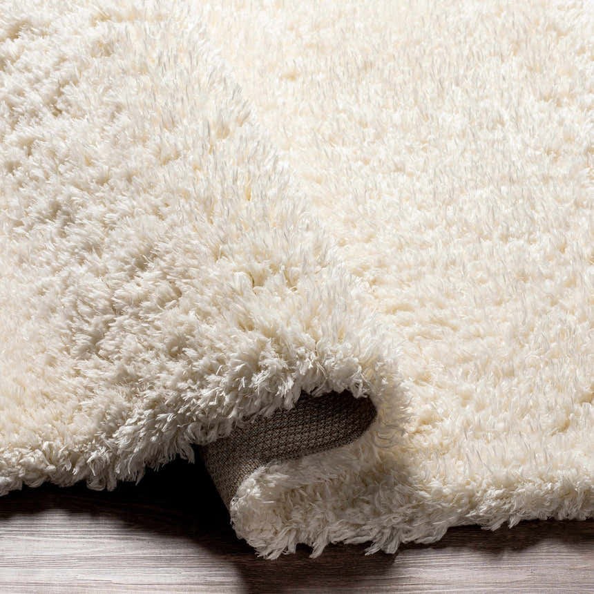 Close-up of the Siari Solid Cream Plush Rug showing its soft, shag texture and woven backing detail. Fold