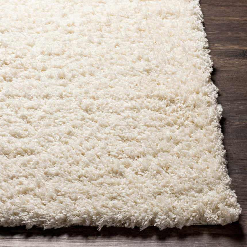Close-up of the plush Siari Solid Cream Rug showing its soft, shag texture on a dark wood floor. Front