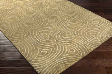 Close up of the Sidney Area Carpet, a hand-knotted wool rug with a geometric pattern in olive and cream on a dark wood floor. Corner