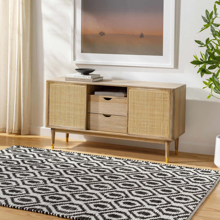Living room scene with a black and white geometric Helmi Area Rug under a wood and cane console table. Roomscene-Rectangle