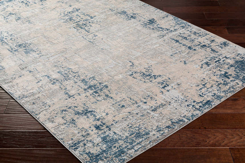 Close up of the Saltair Textured Luxe Rug showing its blue, off white, and gray abstract pattern. Corner