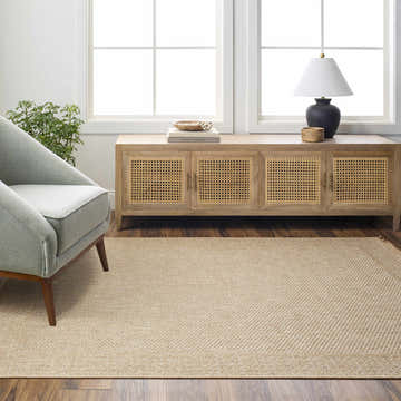 Living room scene with a camel Dorie Indoor & Outdoor Rug, light beige walls, and a gray armchair near a window. Roomscene-Rectangle