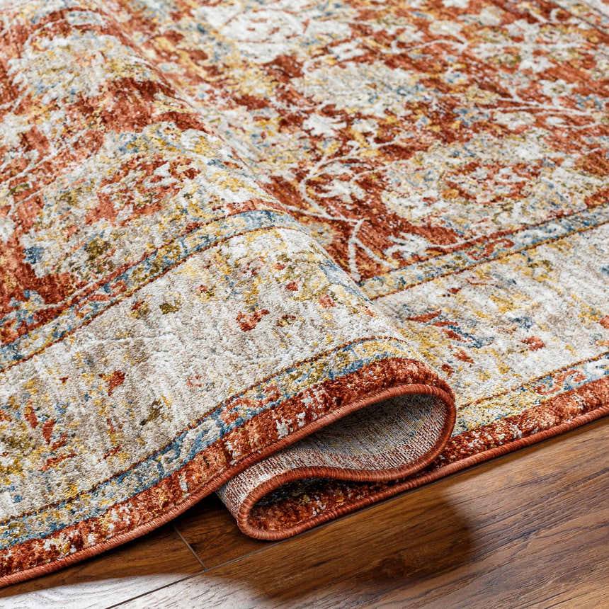 Close-up of the Duong Rust Textured Rug showing brick red, tan, mustard, and blue colors and machine-woven texture. Fold
