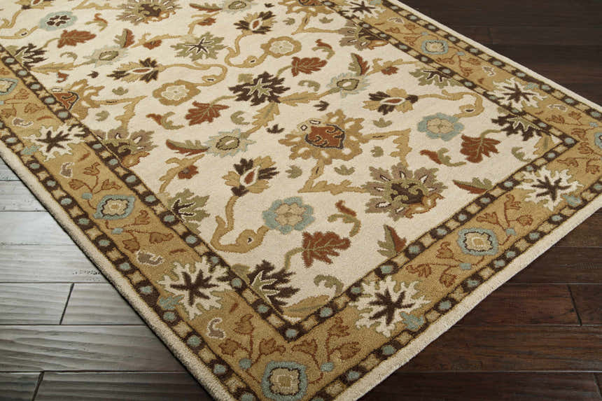 Close-up of the Smoot Area Rug. Beige rug with brown, olive, and blue floral and leaf pattern on dark wood floors. Corner