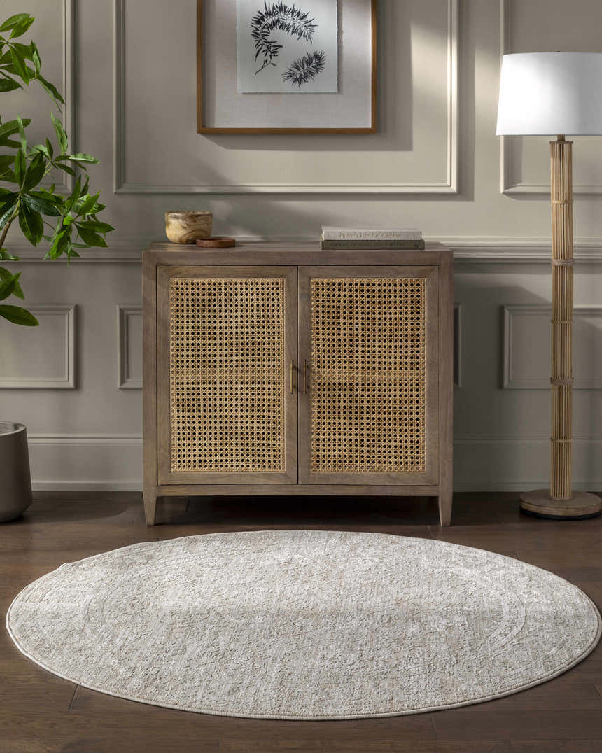 Living room scene with a light gray, round Kyran Area Rug under a cabinet with cane doors. Roomscene-Round