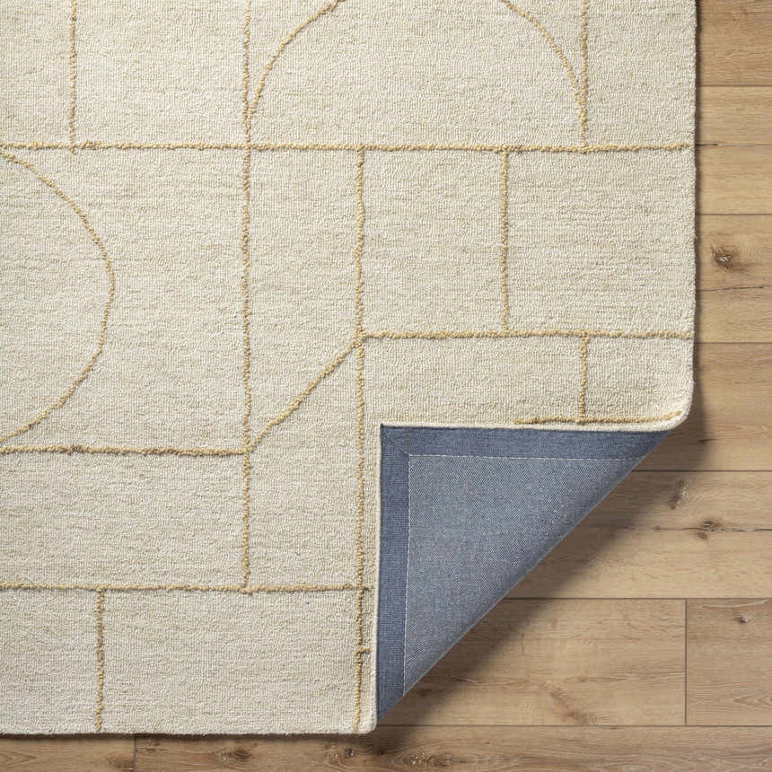 Close-up of the Sanaz Ivory Area Rug. Hand-tufted wool rug with a geometric pattern in ash and tan on a light wood floor. Fold