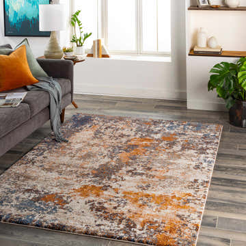 Living room scene with a Santoy Thick Luxe Rug in blue, brown, and cream tones. Gray sofa with orange pillow and wood floors. Roomscene-Rectangle