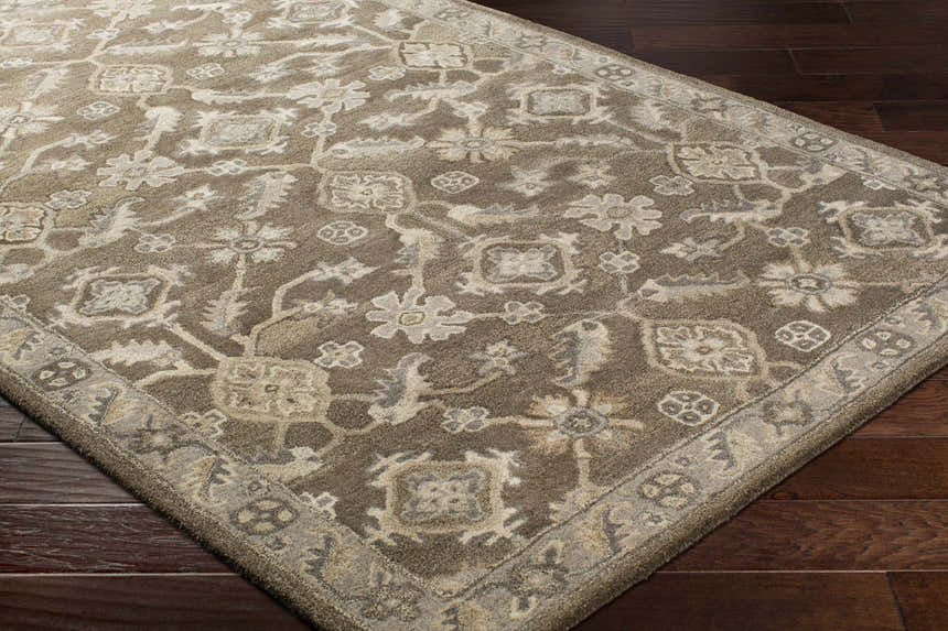 Close-up of the Solen Area Rug. A brown wool rug with a traditional floral pattern and a light beige border on hardwood floors. Corner