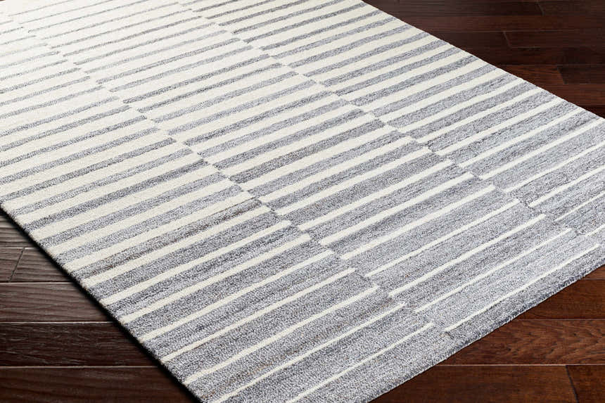 Close-up of Gawel Gray Area Rug showing gray and white stripes on dark wood floor. Contemporary style. Corner