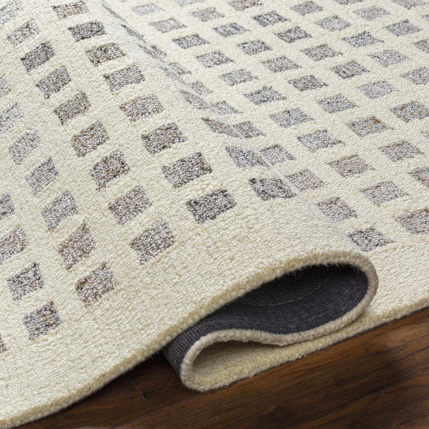 Close-up of the Harib Area Rug showing its beige wool texture and geometric brown and gray square pattern. Fold
